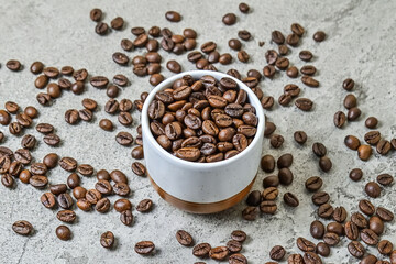 Close up view roasted coffee beans in the ceramic glass or mug. Little, mini. Isolated on gray or gray cement background. Scattered.