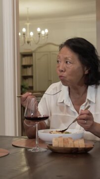 Vertical video: Chinese senior woman at dining table hearing voice, scooping pasta, toasting guest