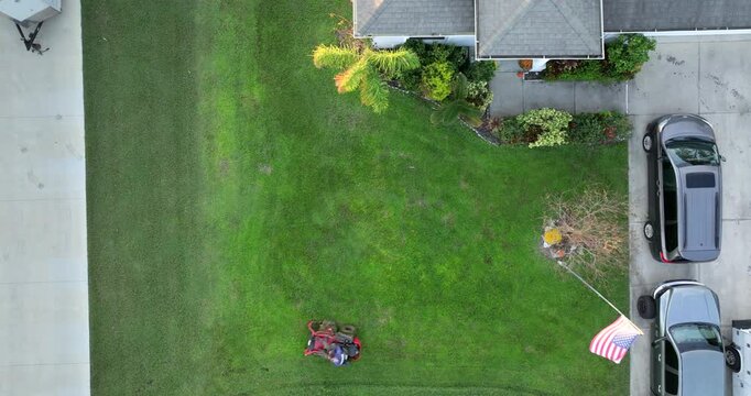 Top view of lawn mowing professional service worker cutting grass in summer with a zero turn lawn mower. Landscaping of rural home backyard.