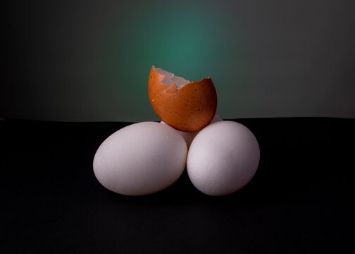 Artistic arrangement of three eggs with a broken shell on top against a dark background.