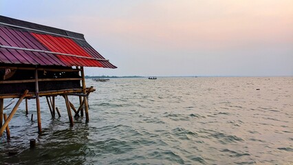 Scenic view of a rustic fishing hut built from bamboo on the ocean shore with boats visible in the distance