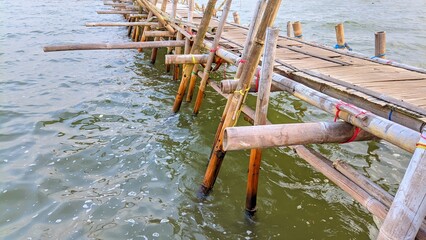Fototapeta premium Traditional bamboo bridge stretching over the sea, serving as fishing spot and rustic dock
