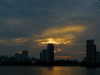 Fototapeta premium Sunset Over City Lake — Golden Reflections and Dramatic Clouds on West Lake in Hanoi, Vietnam