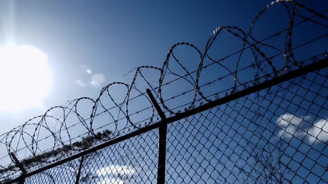 Barbed Wire Fence Against Sunny Blue Sky Symbolizing Security and Restriction in High Contrast Daytime Outdoor Scene