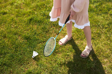 Girl holding badminton racket preparing to hit shuttlecock on grass outdoors, wearing summer dress...