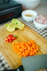 Fresh raw cooking ingredients, chopped carrot, lime, and meat on wooden cutting board.