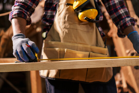 Black carpenter working in woodworking factory, carefully inspecting a wooden plank after cutting. Concept of craftsmanship, labor, and skilled profession.