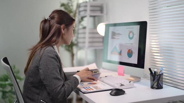 A woman is sitting at a desk with a computer monitor in front of her. She is drawing a graph on the screen