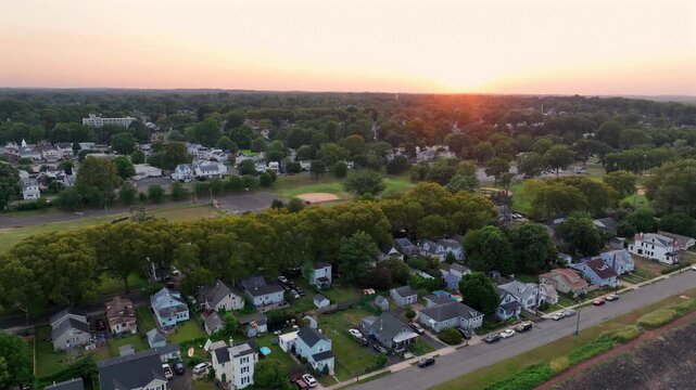 American houses and homes in row during golden sunset in Trenton, New Jersey. Sportive baseball field and buildings in suburb of city. Descend drone wide shot. Peaceful scene in the evening.