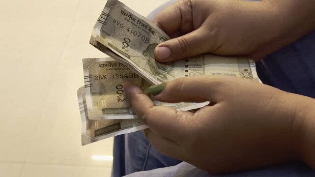 closeup of a women's hand counting an 500 rupee note of indian currency at the bank