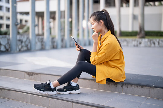 Smiling young Asian woman using digital tablet in urban city