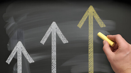Hand drawing upward trend arrows on chalkboard symbolizing business growth and success, achieving goals