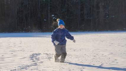 Kid in snowy winter park. Winter child plays with snowflakes. Kids winter holidays. Childhood...