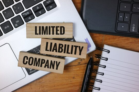 Wooden blocks reading 'Limited Liability Company' on a desk with laptop, notebook, and pen, representing business organization and entrepreneurship.
