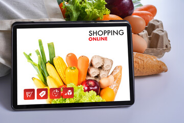 Online grocery shopping concept showing fresh vegetables, fruits, bread, and eggs on a tablet screen, illustrating how consumers buy healthy food via e-commerce and fast delivery services.