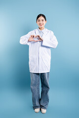 Caring medical worker in lab coat and jeans makes a heart shape with her hands on blue background