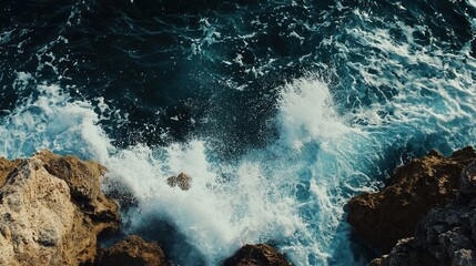 Obraz premium Waves crash powerfully against rugged, rocky cliffs. The water is a deep, turbulent blue-gray, with white foam and spray erupting as the waves break.