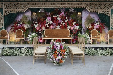 A Stunning Display of Wedding Flowers in Bright Shades of Red, Orange, and Pink, Arranged Gracefully Beside Classic Wooden Chairs