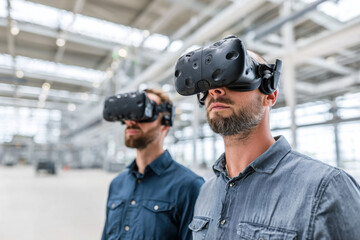 Engineers with VR headsets in an empty industrial space, simulating machinery control, concept of virtual prototyping and design