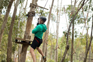 Man wearing helmet and harness navigating high-rope cables and obstacles in woodland adventure park