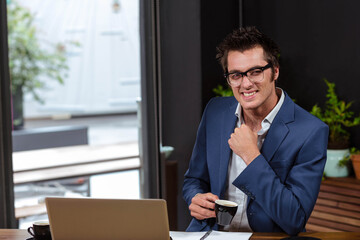 Naklejka premium Businessman adjusting shirt collar while sipping espresso at coffee shop with laptop and pen