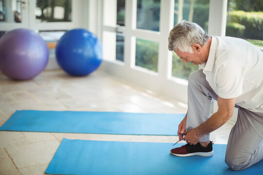 Fototapeta Man kneeling tying sneaker laces on mats in home gym with stability balls near windows