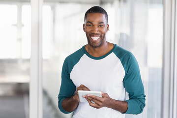 Man standing and using white tablet in office corridor, with glass partitions and natural light