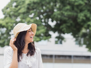 Hispanic woman smiling while wearing white blouse touching straw sun hat outdoors, copy space