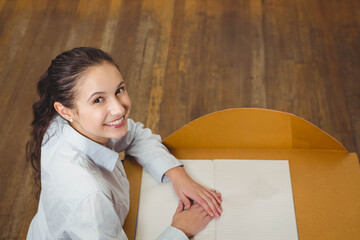 Woman wearing white blouse sitting at wooden desk smiling at camera with open notebook, copy space