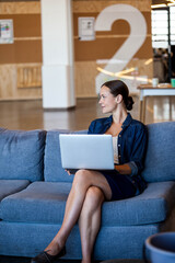 Silver laptop sitting on blue couch in modern office lounge near wood-paneled wall, copy space