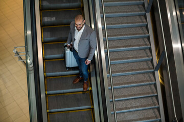 Man standing on down escalator with glass rail at terminal holding suitcase in blazer, copy space