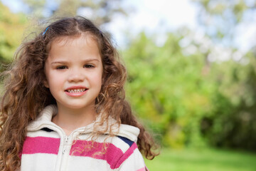 Female child standing in lush garden wearing striped zip-up sweater with hair clips, copy space