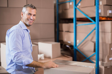 Man in his forties packing cardboard boxes at warehouse table with tape dispenser, copy space