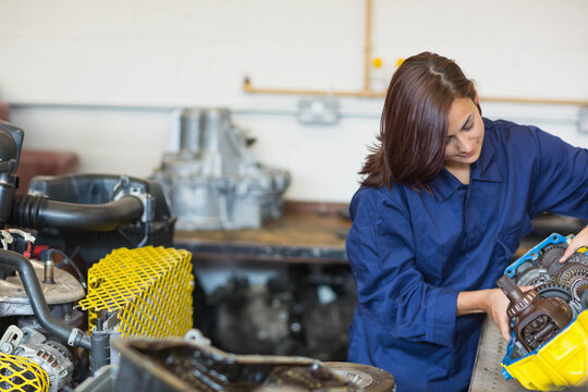 Woman in coverall examining gearbox housing at workbench with gears and safety guard, copy space - Powered by Adobe
