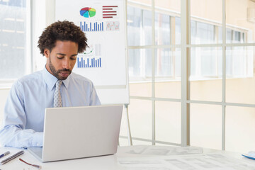 African American man wearing shirt and tie working on laptop at office reviewing flip chart