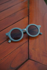 Stylish round-framed sunglasses sit on a polished wooden table. This image captures the essence of summer, leisure, and trendy accessories