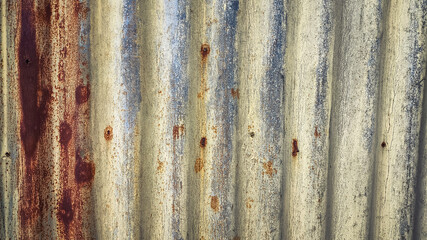 Aged zinc fence wall with rusty patterns and faded textures. Vintage corrugated metal panel ideal for background use, industrial decay themes, or rustic material surface applications.