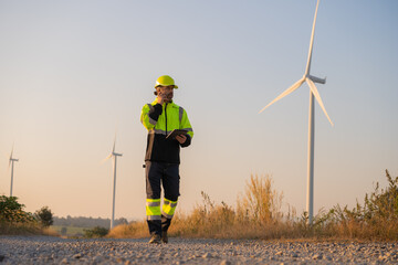 Engineer working on laptop in front of wind turbines for checking wind turbines of the field during beautiful sunset. Alternative energy concept.