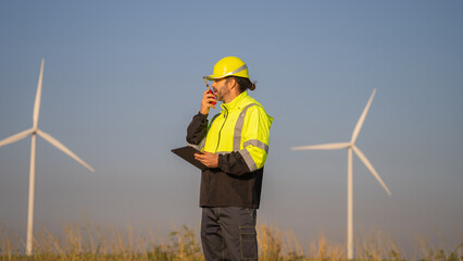 Engineer working on laptop in front of wind turbines for checking wind turbines of the field during beautiful sunset. Alternative energy concept.