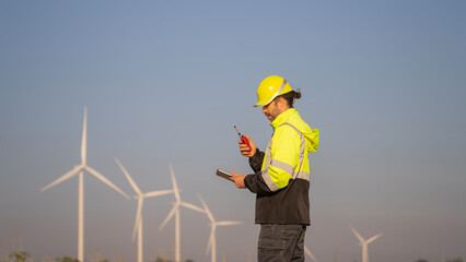 Engineer working on laptop in front of wind turbines for checking wind turbines of the field during beautiful sunset. Alternative energy concept.