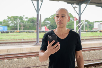 Obraz premium Portrait of Hispanic tourist man at train station platform using mobile phone