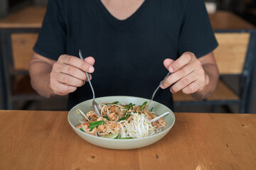 Tourist man eating Pad Thai noodles outdoors at local Asian food court