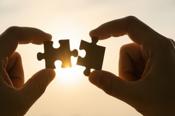 Hands Holding Two Puzzle Pieces Against a Bright Sunset, Symbolizing Connection, Teamwork, and Problem-Solving in Personal and Professional Life