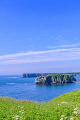 Scenic summer landscape from Cape Azechi in Hamanaka Town, Hokkaido, Japan. The viewpoint offers a wide view of Hamanaka Town, Kenbotsukito Island, small islets, and the Pacific Ocean under a clear bl