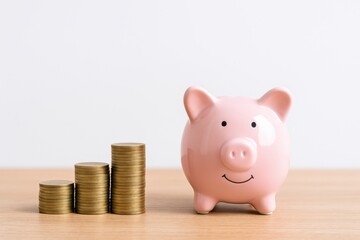 Cute pink piggy bank next to stacks of golden coins representing savings, financial planning, and wealth management for personal finance concepts