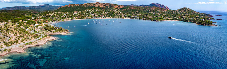wide angle aerial landscape view of French Riviera coastline along Agay Bay in Saint-Raphaël with Plage d'Agay and Plage de La Baumette, boats anchored in bay, wooded hilly landscape in background