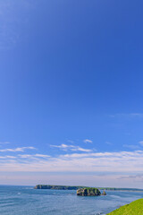 Scenic summer landscape from Cape Azechi in Hamanaka Town, Hokkaido, Japan. The viewpoint offers a wide view of Hamanaka Town, Kenbotsukito Island, small islets, and the Pacific Ocean under a clear bl