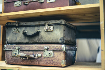 Several old vintage suitcases lie on a wooden shelf on top of each other. Vintage rivet handles and...