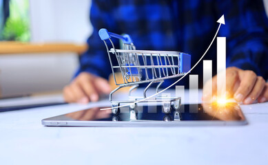 e commerce concept with a man pointing on tablet screen and small cart to show graph increase...