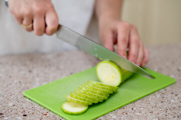 Close-up of hands slicing zucchini with a knife on a green board, concept: fresh meal preparation...